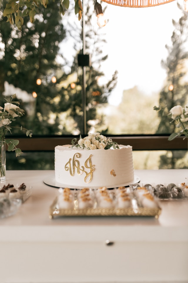 Bolo branco com monograma dourado e decoracao floral, ideal para festa de 50 anos